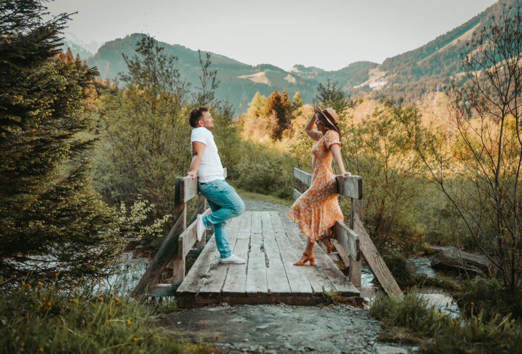 Couple poses together on a wooden bridge in Switzerland, surrounded by spring wildflowers and mountains