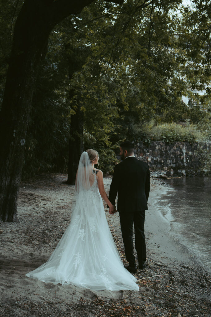 A couple walks on a private beach holding hands and looking into each other's eyes after their wedding ceremony in Switzerland