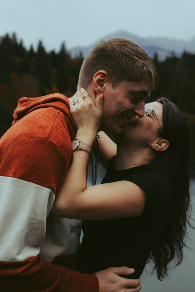 During their couples photoshoot in Switzerland, a girl holds her boyfriend's neck as she gently leans in for a kiss