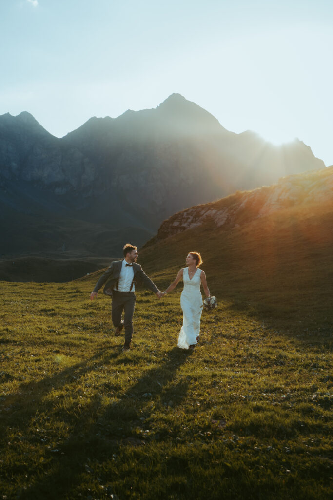 Couple running in a swiss mountain meadow during golden hour during their elopement
