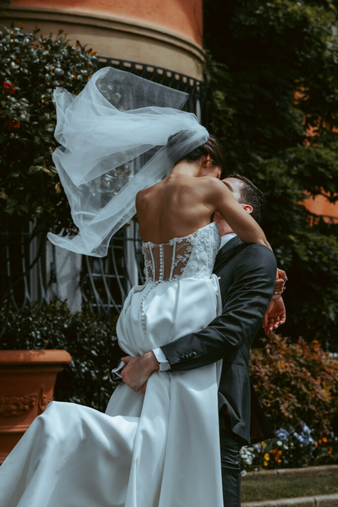 During their wedding in Switzerland, a groom holds his bride in his arms and twirls her around, as her veil blows beautifully in the wind and she holds her arms around his neck