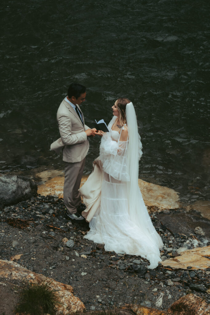 A couple reads their vows to each other while standing in front of a small alpine lake, fed by a waterfall