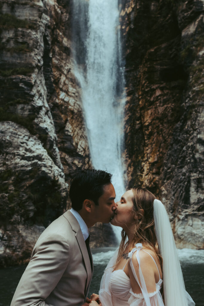 A couple kisses in front of a waterfall during their elopement day in Switzerland