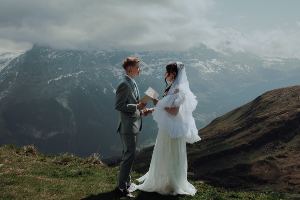 A couple stands facing each other and reading their vows to each other during their elopement amongst the swiss mountains