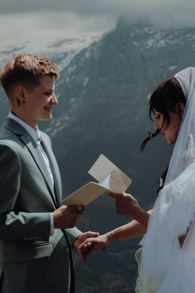 In Grindelwald, an eloping couple stands in front of swiss mountains and a glacier, as they read their vows to each other