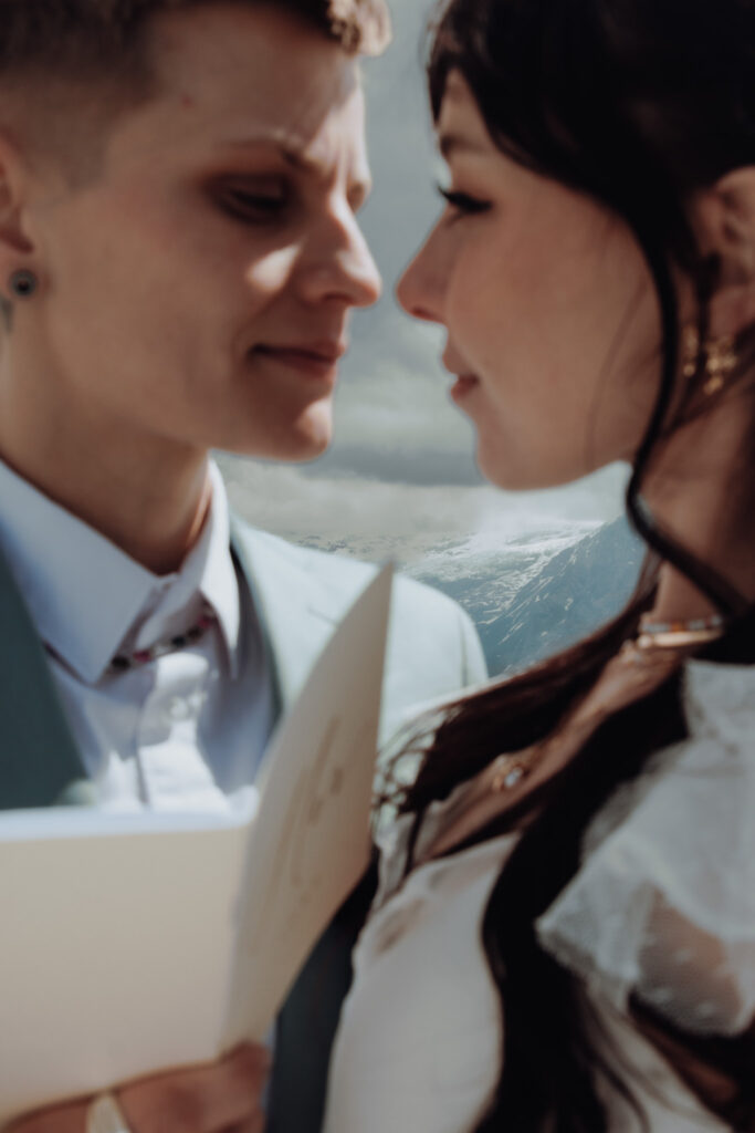 Close up portrait of two brides' faces as they look into each other's eyes, and one holds her vow booklet, during their elopement in Grindelwald (Switzerland)