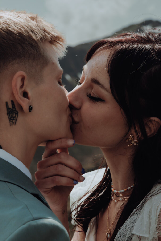 A couple kisses during their elopement in Grindelwald (Switzerland) amongst the mountains. One woman holds the other woman's chin gently as she leans in for the kiss