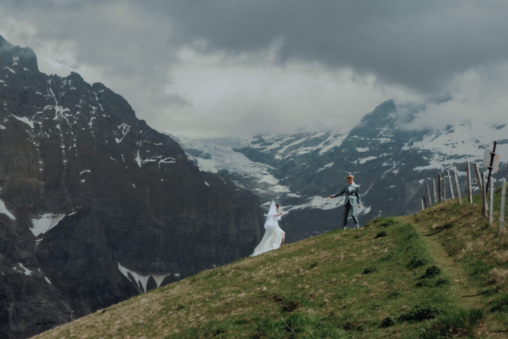 During their elopement in Grindelwald (Switzerland), a couple walks in the distance, holding hands and moving towards the swiss mountain peaks that are in the background