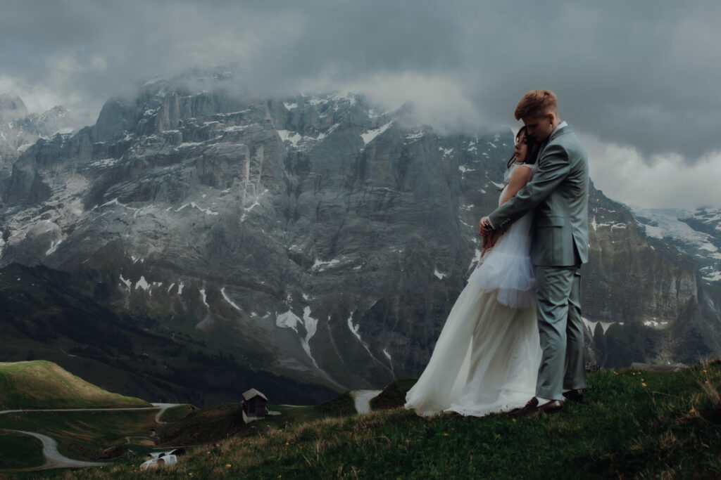 During their elopement in Grindelwald (Switzerland), two women hold each other, as one woman's wedding dress blows in the wind and mountain peaks can be seen behind them