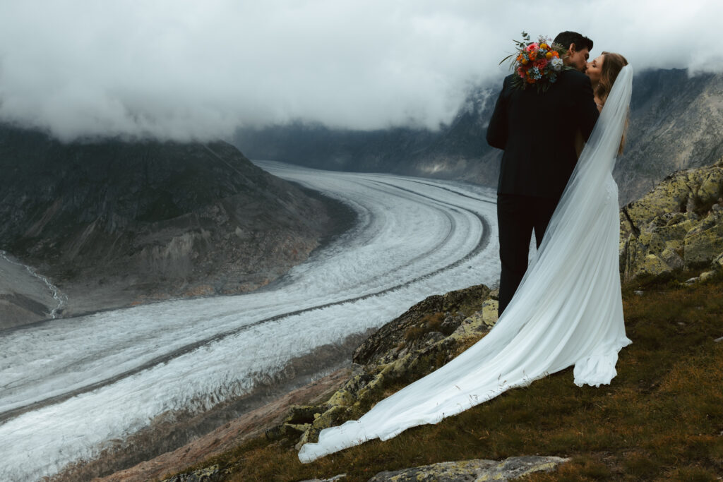 During their glacier elopement in the Swiss Alps, a couple leans into a kiss as they pose in front of a Swiss glacier