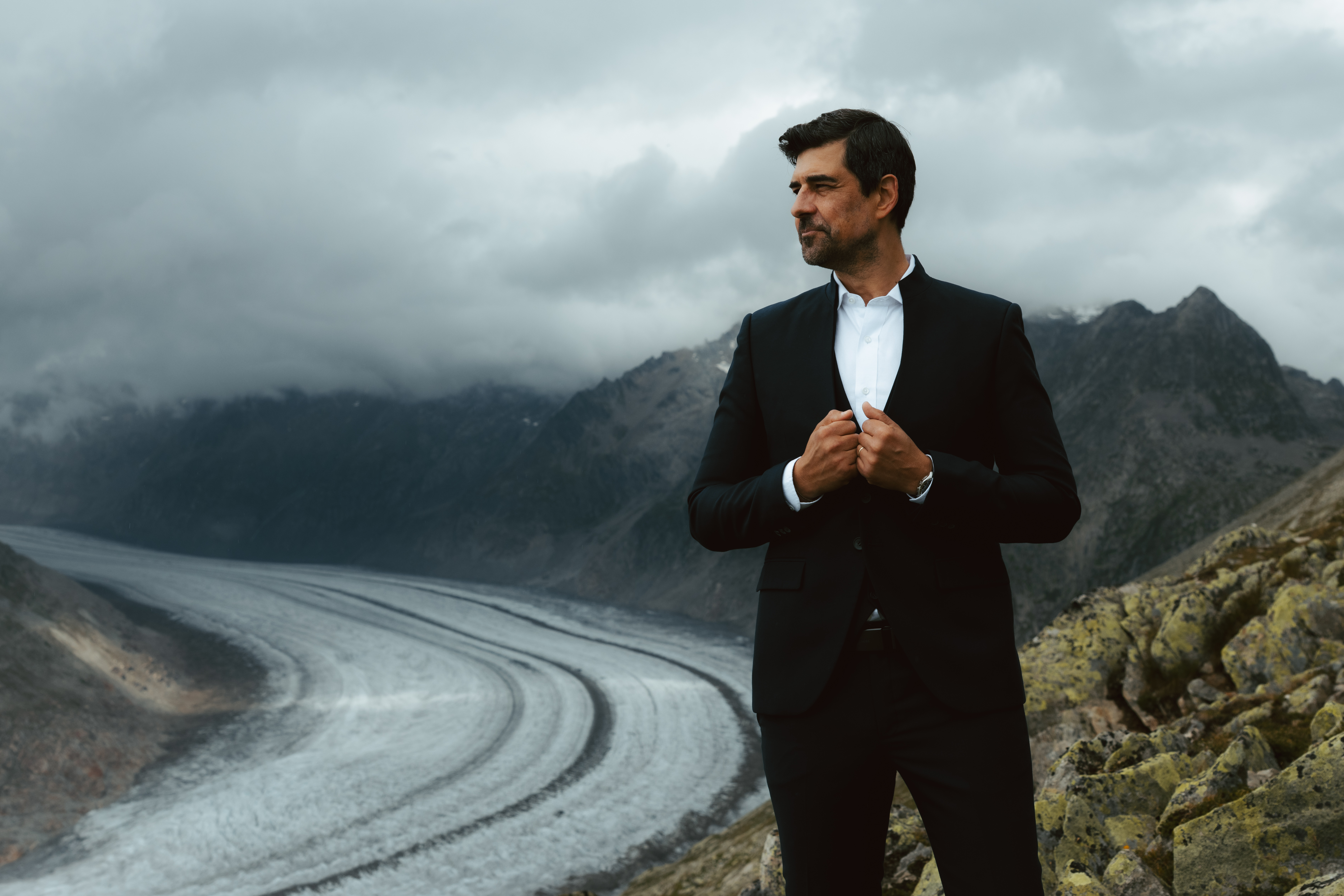 A groom holds his hands on his chest as he looks out towards a glacier during his elopement in Switzerland