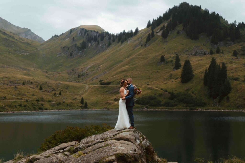 A couple stands on a rock in front of a swiss mountain lake and embraces each other during their elopement in Switzerland