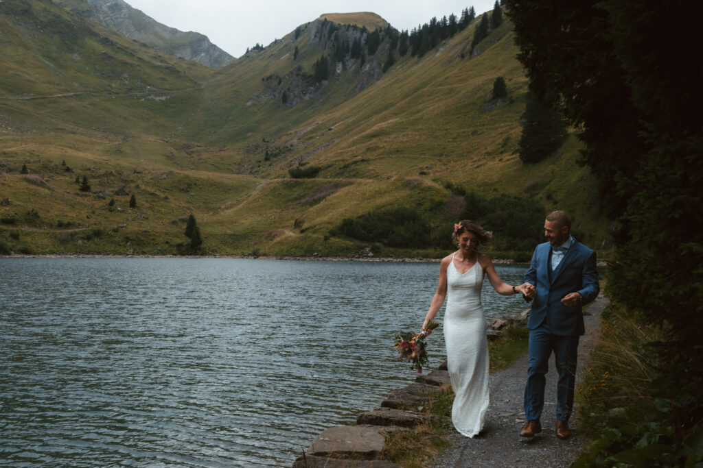 A couple walks on the side of a mountain lake nestled in the Swiss alps
