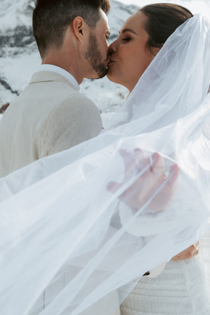 Close up of a couple kissing and the bride's veil blowing in the wind during their snowy elopement in switzerland