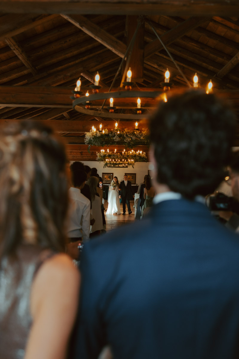 A groom and his mother look at the bride walking down the aisle