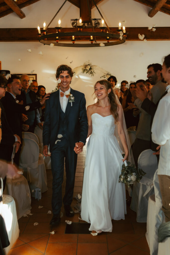 A couple walks down the aisle during their wedding as their guests throw white rose petals around them