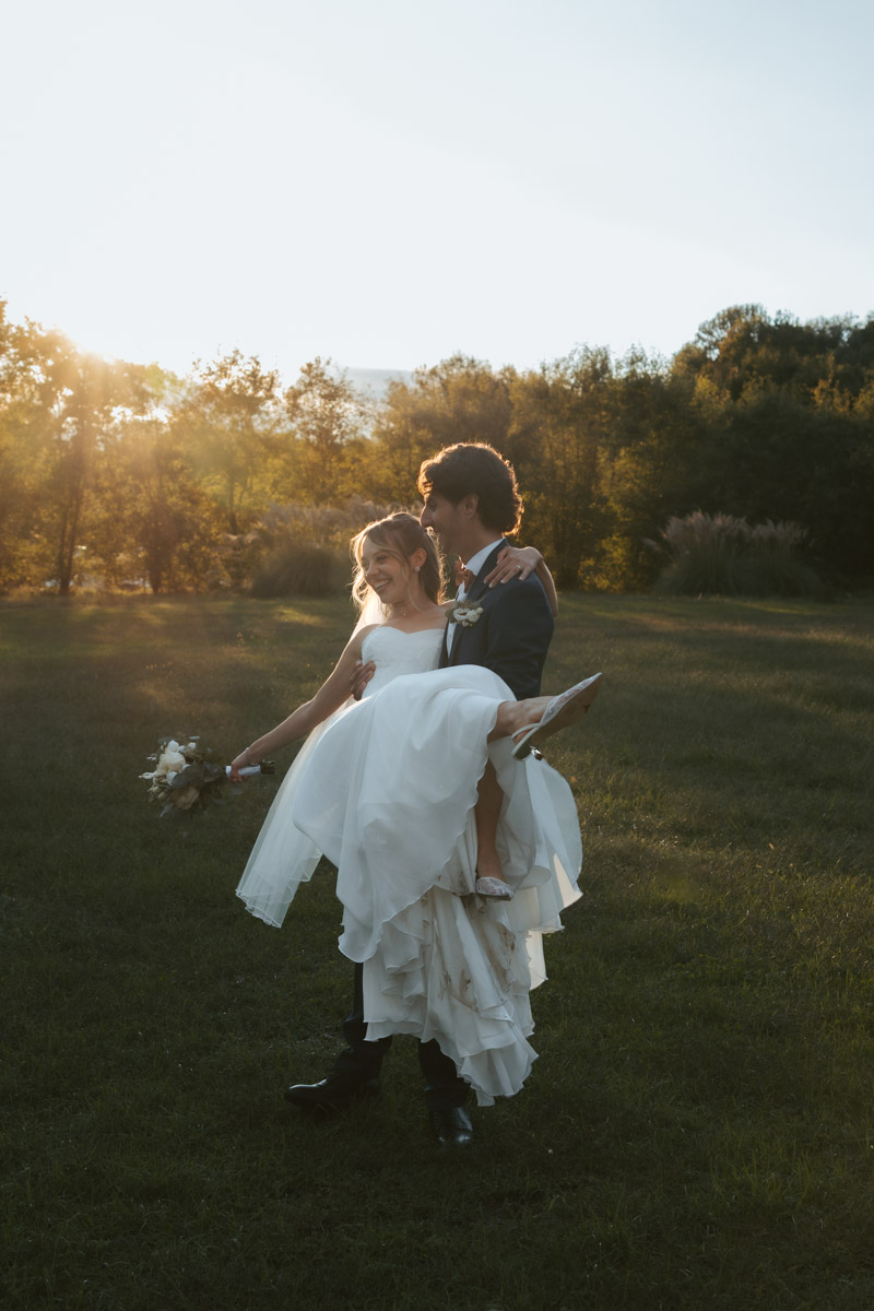 A groom lifts his bride in the air and twirls her during golden hour