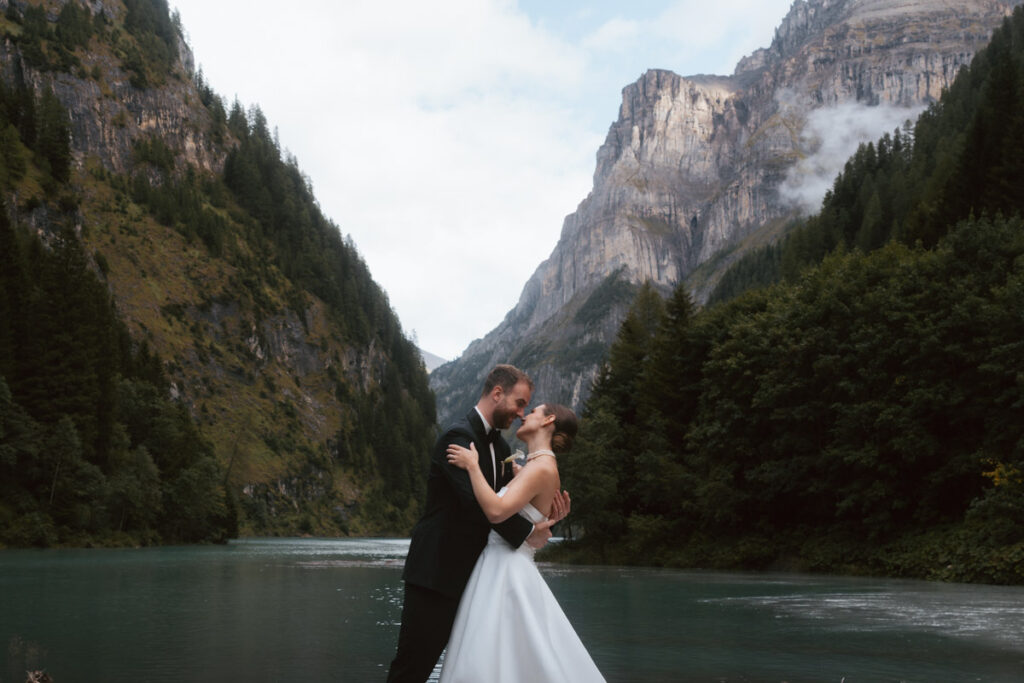 A couple stands in front of the swiss alps and a turquoise lake during their elopement in Switzerland