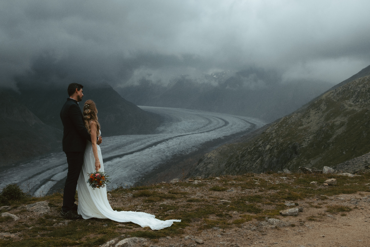 A couple looks at a glacier during their Swiss mountain adventure elopement