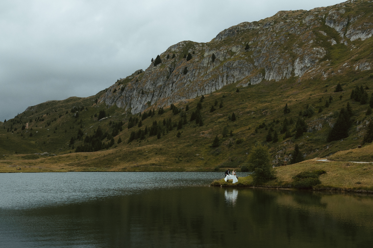 During their elopement in Switzerland, a couple stands by a distant lakeshore, surrounded by the Swiss Alps