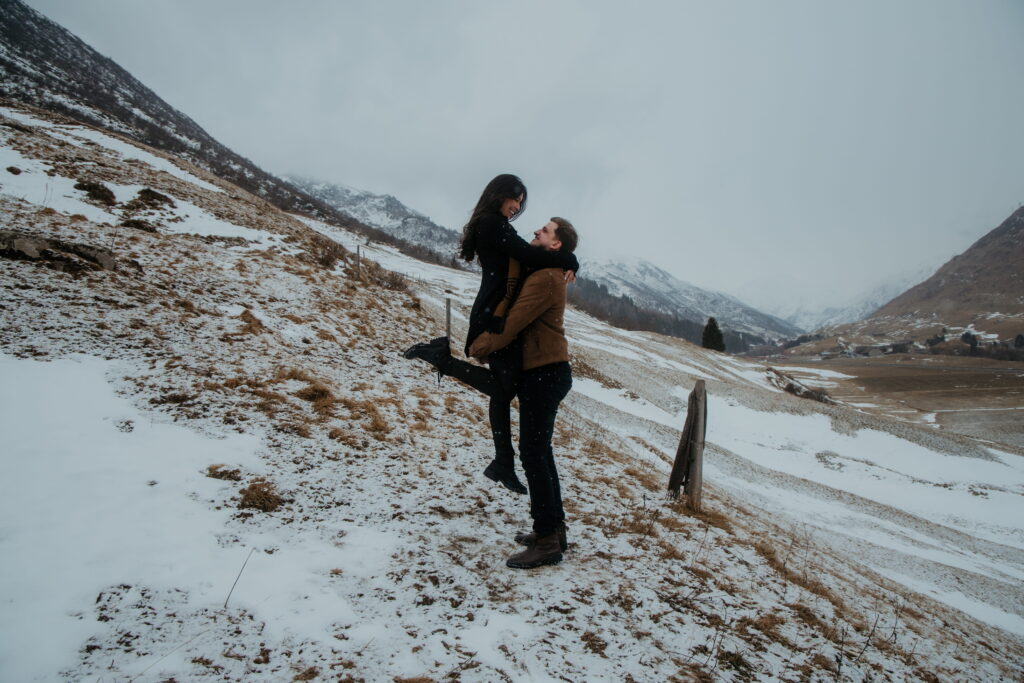 A man lifts his girlfriend up in the air in the snowy mountains of Andermatt