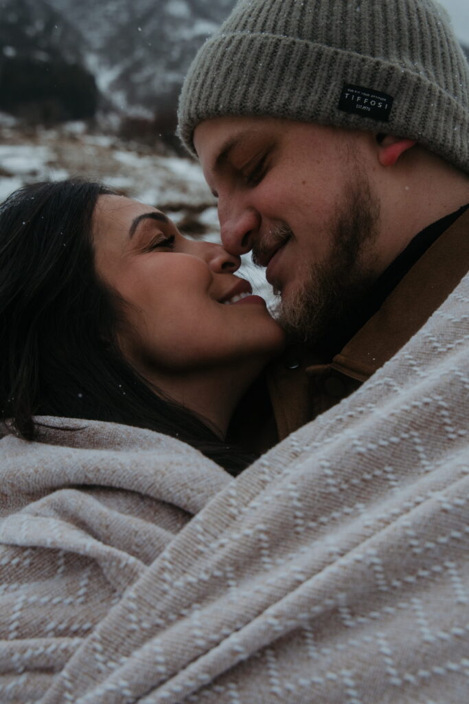 A couple embraces, wrapped up in a blanket in the snow covered mountains of Andermatt