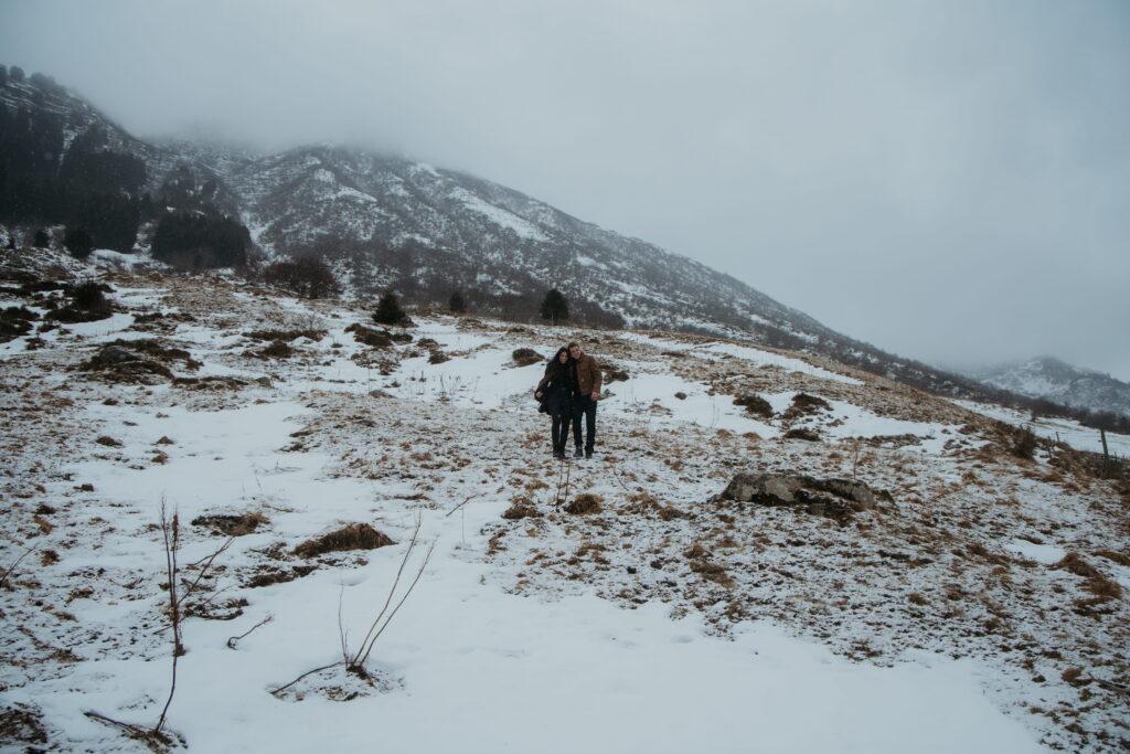 Wide shot of couple running through the snowy mountains in Andermatt